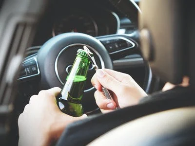 A person opening a beer bottle while driving