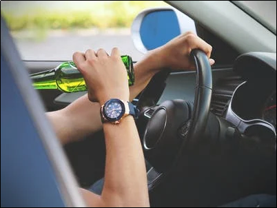 A person drinking beer while driving that will soon need SR22