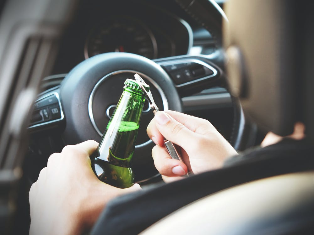 person opening a bottle of alcohol while driving